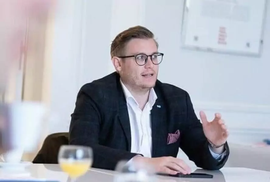 Ein Bild auf 5min.at zeigt Gemeinderat Julian Geier, er trägt Anzug und eine schwarze Brille. Vor ihm steht ein Glas Orangensaft.